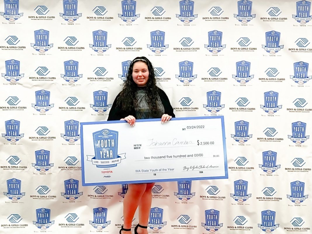 Boys and Girls Clubs of Skagit County 2022 Youth of the Year Johanna Gamboa stands with a large check in front of a step and repeat