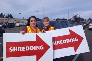 two women in construction vests holding big signs with red arrows that say 'this way' for the BECU shred event