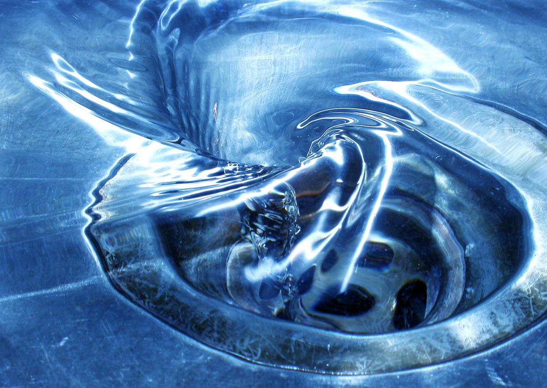 close up of water going down a drain in a steel sink