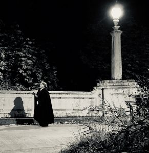 women in black walking by a street lamp