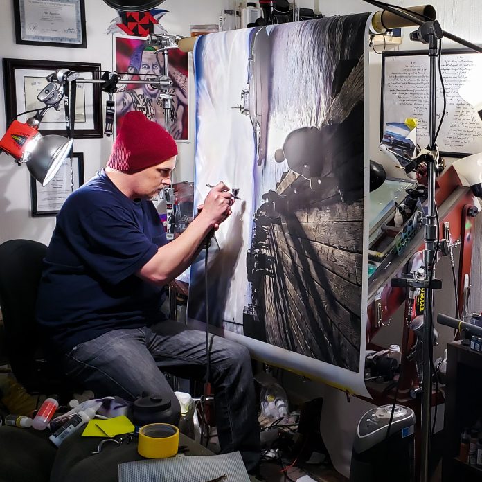 Joel Aparicio airbrushing a large military-themed painting