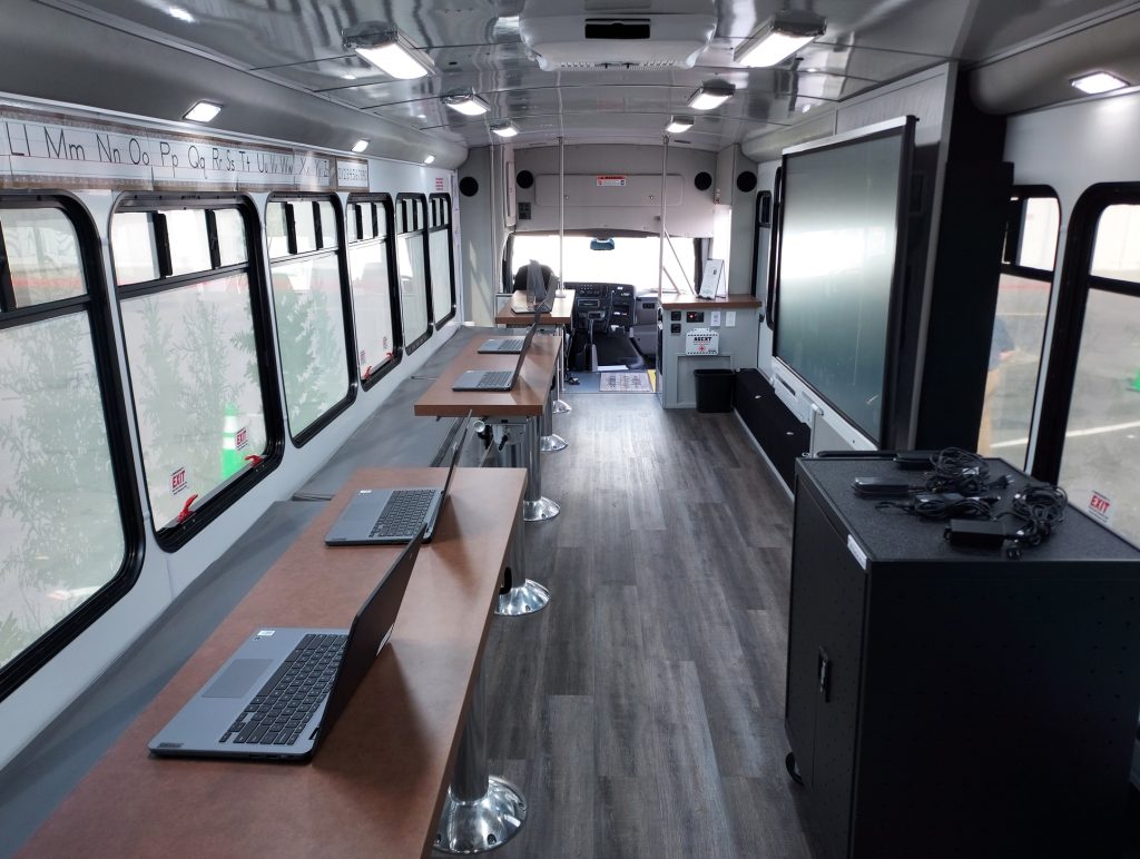 Goodwill's Digital Equity Bus with a long table with laptops on it and a big screen on the other side