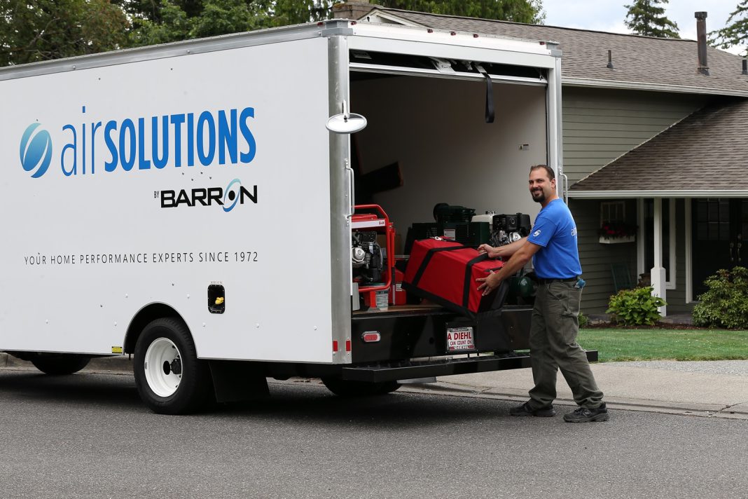 Barron worker in a blue shirt puts a large red machine into the back of a truck that has the words, "Airsolutions - Barron. Your home Performance experts since 1972'