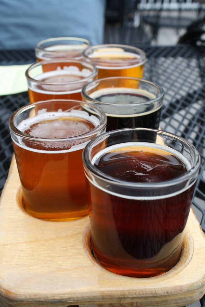 six small beer glasses full of beer inside a wooden tray