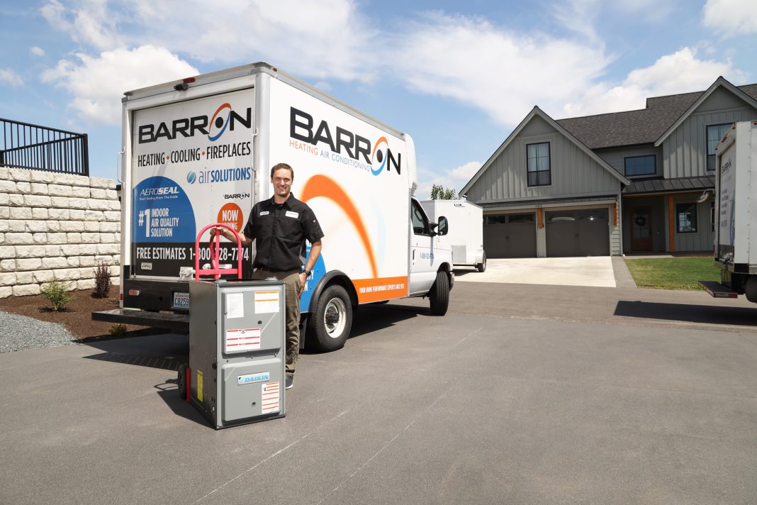 Barron Heating AC Electrical & Plumbing worker next to a Barron truck with a HVAC on a hand truck.