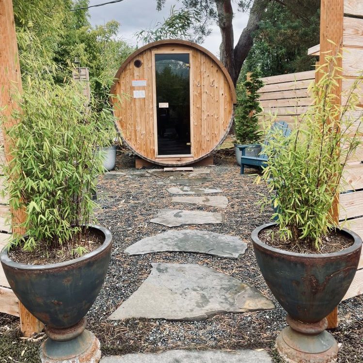 barrel sauna with two plants in planters and a stone path