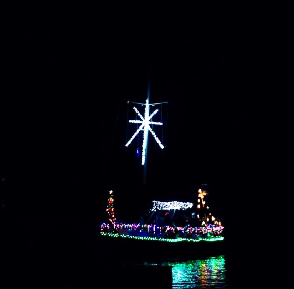a boat on the water at night lit up with christmas lights and a large star on it's mast