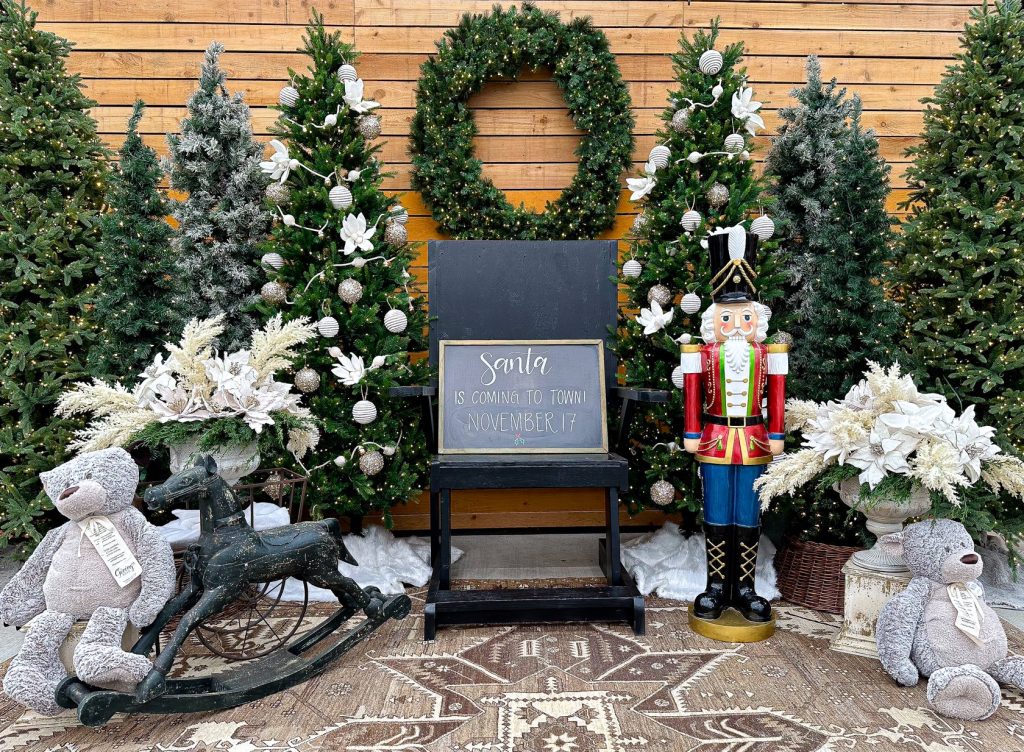 lots of evergreen trees, wreaths by a wooden wall with a rocking horse, a chair and a nutcracker in front of it.