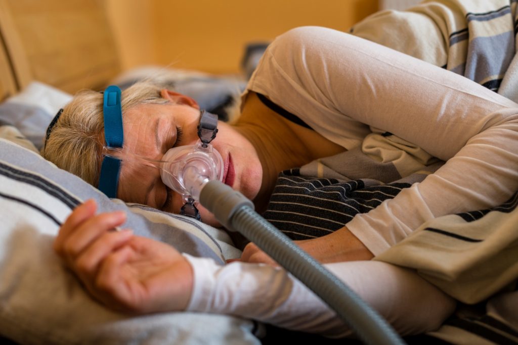 a woman lying on her side on a bed with a CPAP machine attached to her
