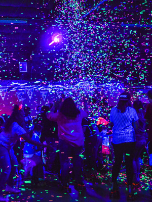 People roller skating under black lights while confetting is falling at Skagit Skate.