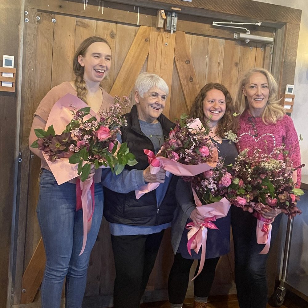four women standing for a photo, three of them are holding bouquets of flowers