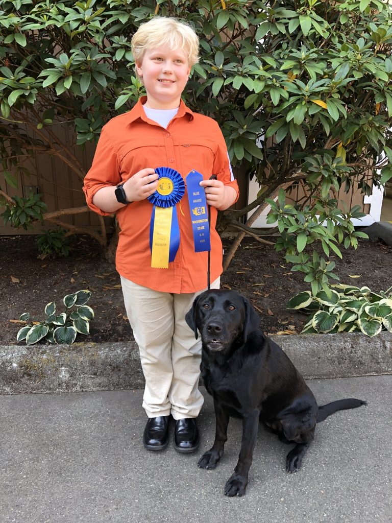 Patrick swan with his black lab posing for a photo, he is holding two award ribbons