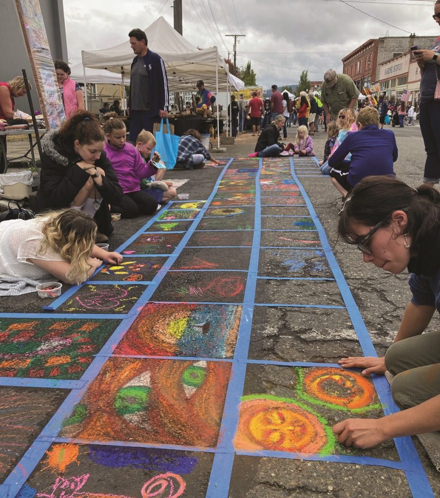 people of all ages drawing art on the sidewalk in taped off squares