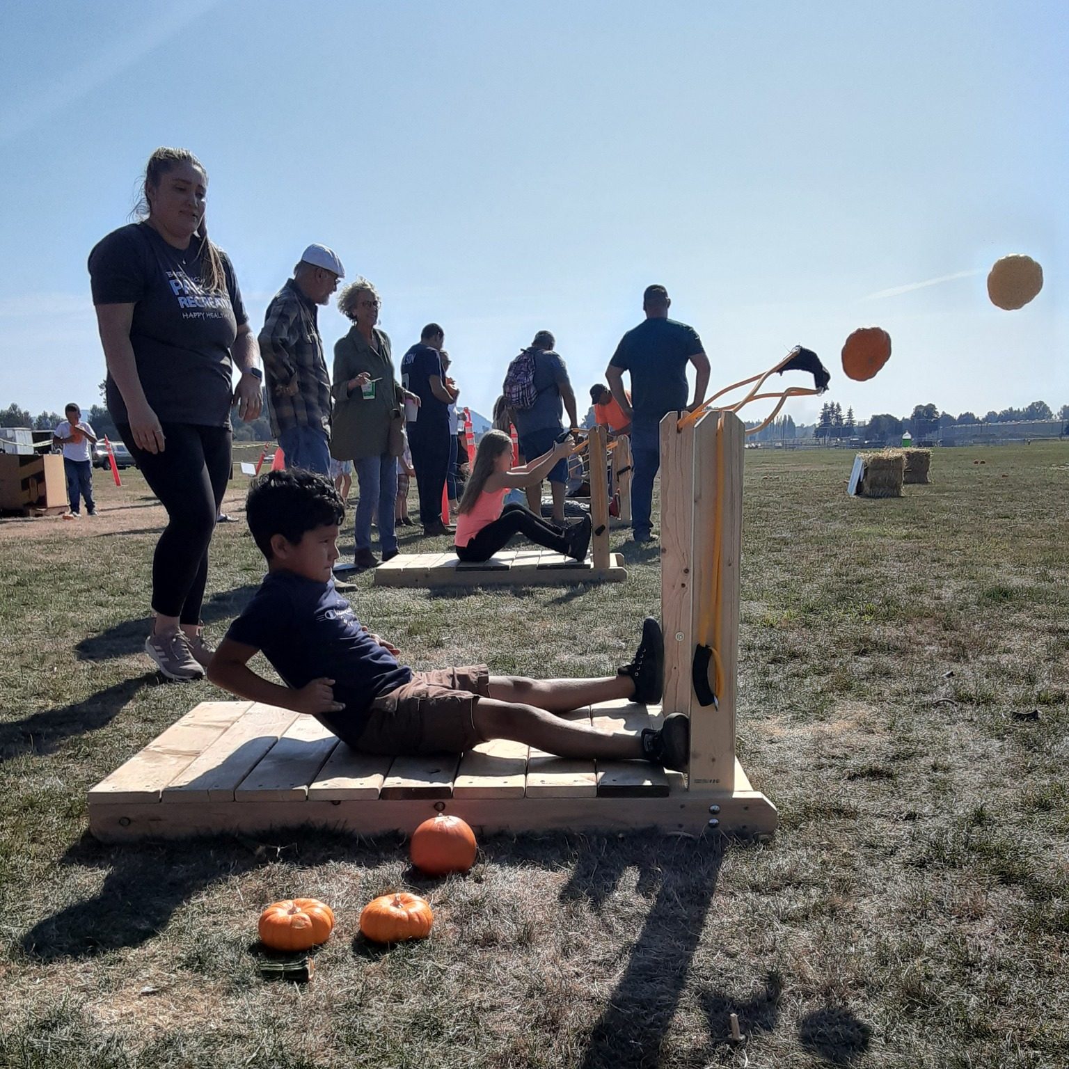 a kid sitting on a wooden platform launching a pumpkin for a giant sling