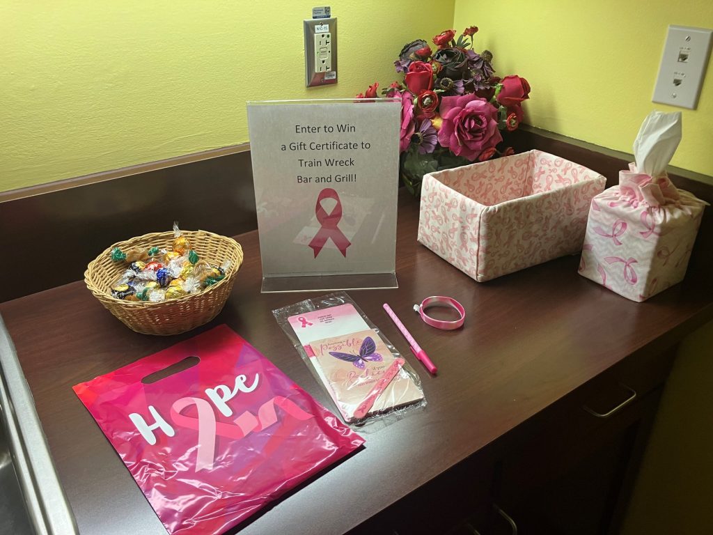 gift items on a table with a pink bag with the breast cancer ribbon on it