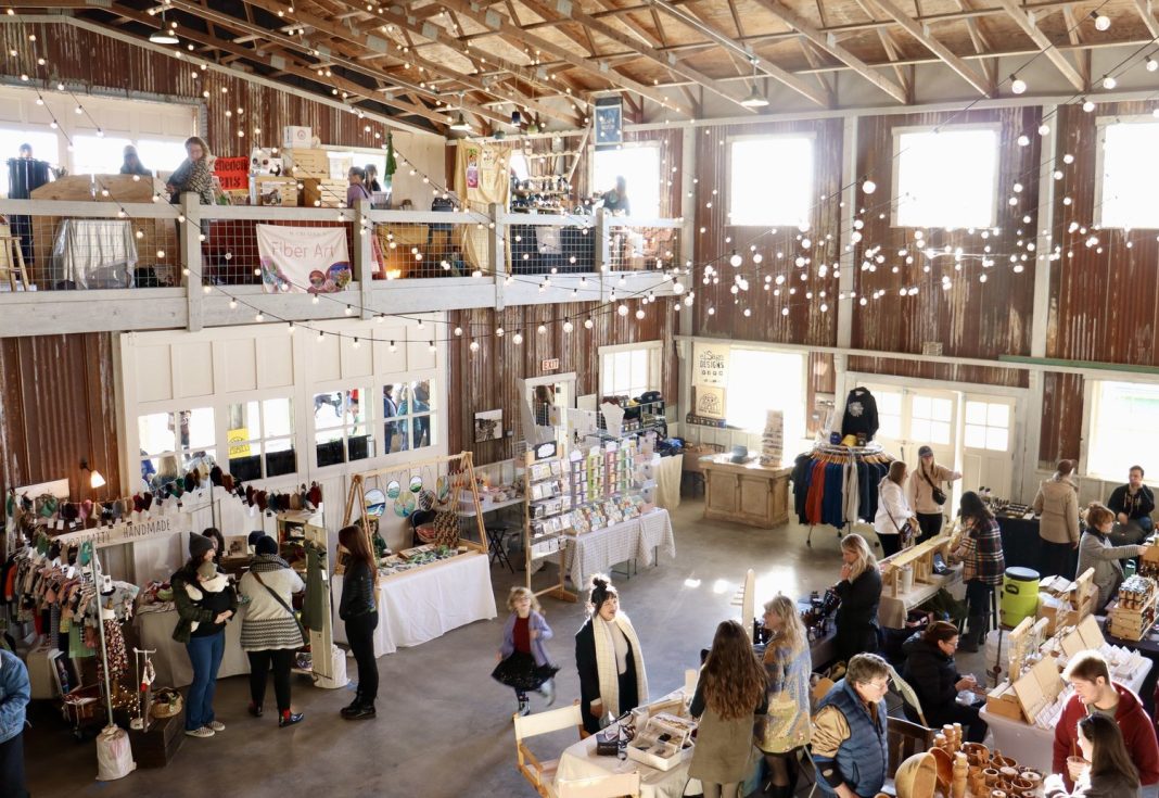 large room with white lights, fake snowflakes and tables full of things for sale. People are walking around