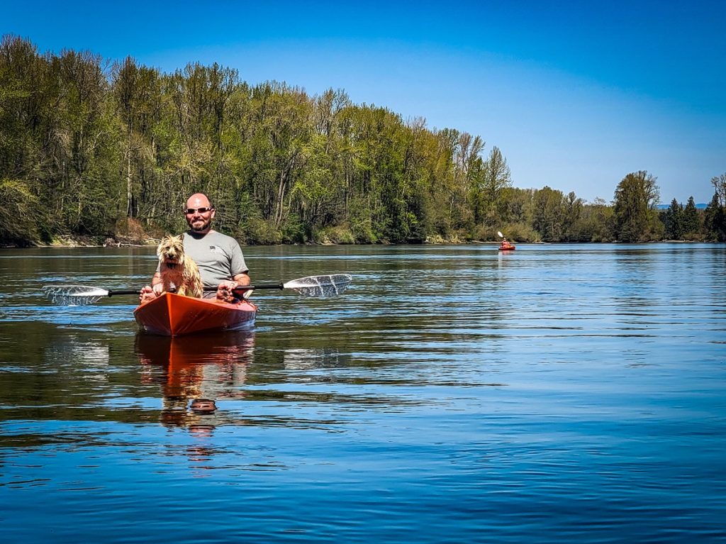 Kirk Knudsen sitting in a red kayak with a little dog in front of him on the Skagit RIver