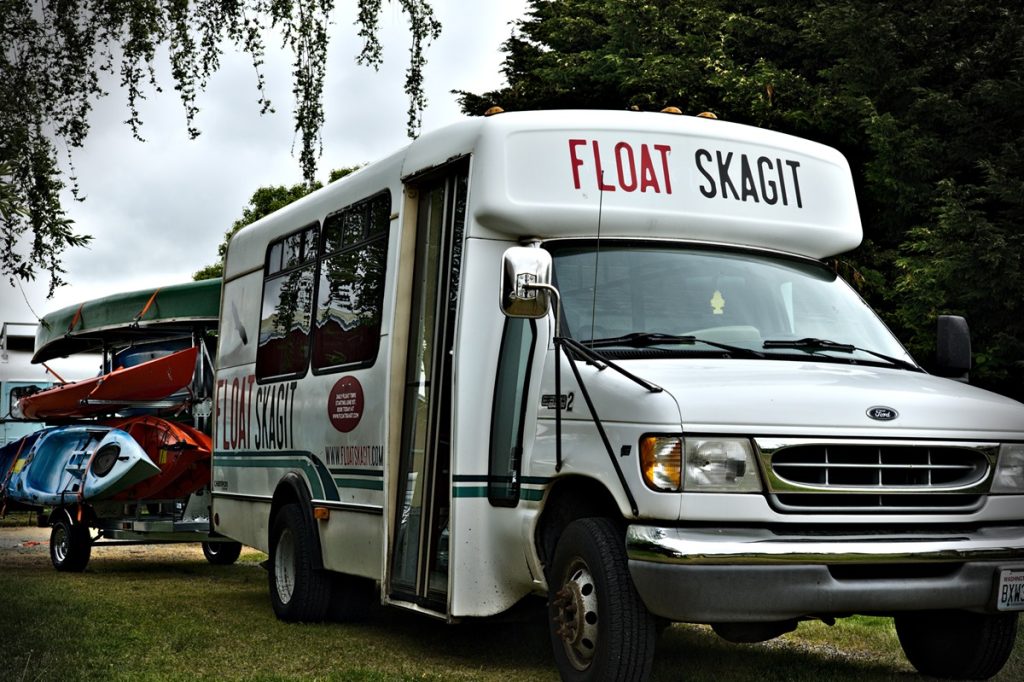 Transit Van with "Float Skagit: across the front above the cab. Attached is a trailer with kayaks.